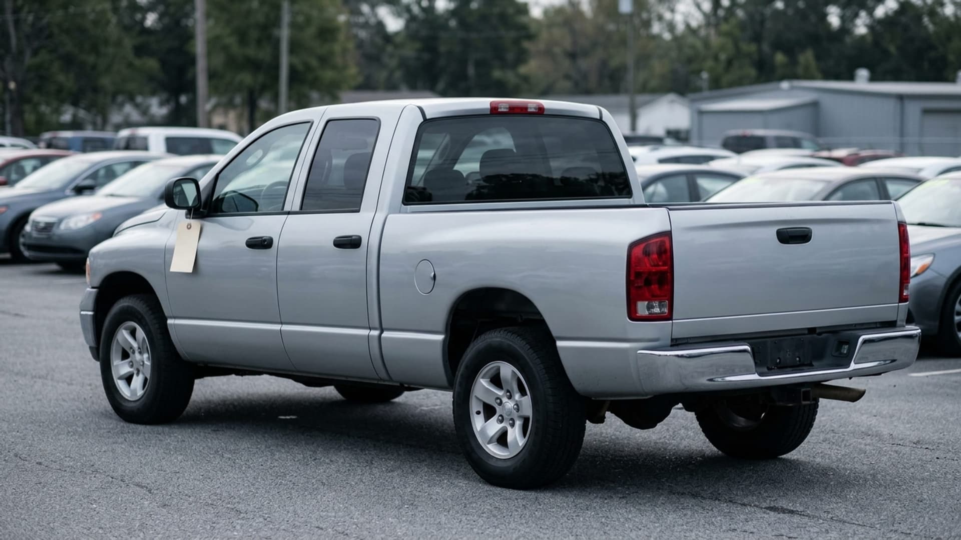 A silver pickup parked at the edge of an independent lot in morning light with a blank key tag on its side mirror.